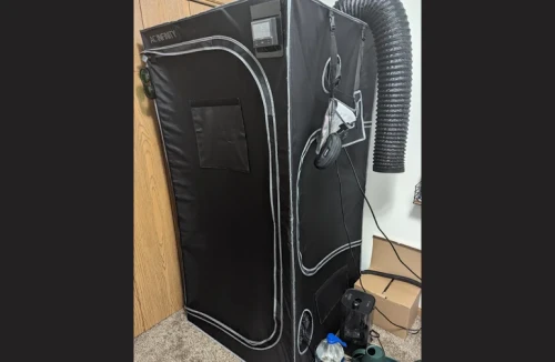 An exterior view of an AC Infinity grow tent with black fabric walls sucking inward due to negative pressure. A digital environmental controller is mounted on the top and black ducting exits the side.