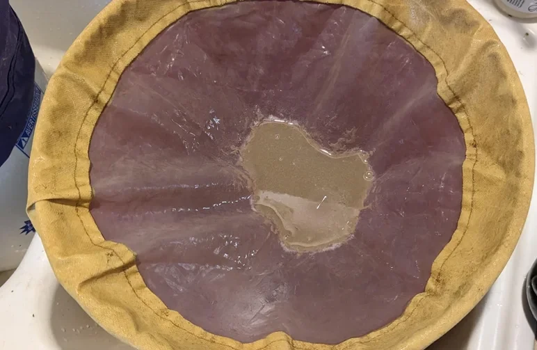 Nahaufnahme von nassem, blondem Ice-Water-Hash, das vom unteren Mesh eines gelben Bubble-Bag-Filters gesammelt wird.
