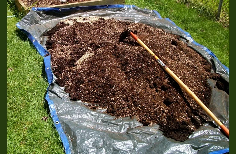 Großer Haufen organischer Cannabis-Super-Soil, der von Hand auf einer blauen Plane mit einer Gartenhacke gemischt wird, um Zusätze und Belüftung zu vermengen.