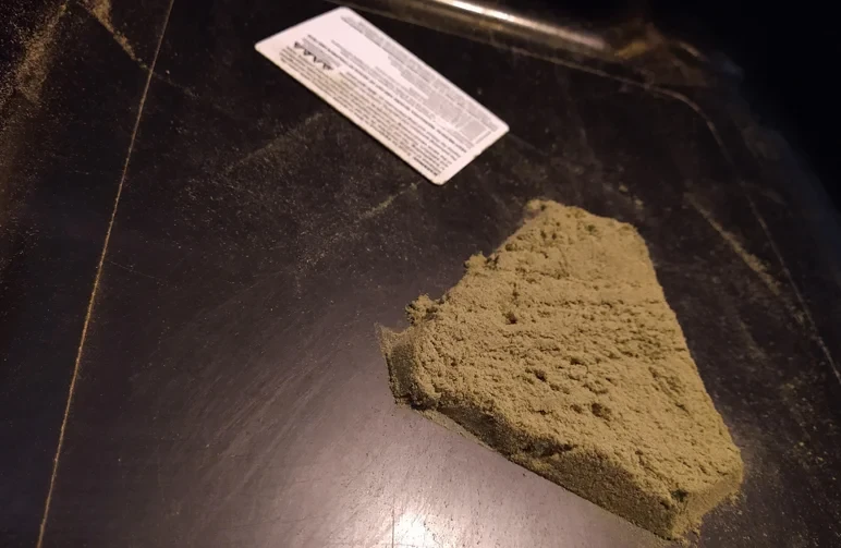 Ein großer, dreieckiger Haufen sandig-blonden Kiefs, gesammelt auf einem schwarzen Siebtray, mit einer Kunststoffkarte zum Abschaben.