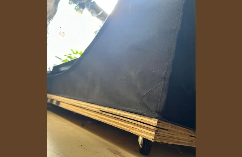 A close-up of a black grow tent elevated off a cold basement floor using a custom plywood platform on wheels to provide insulation.